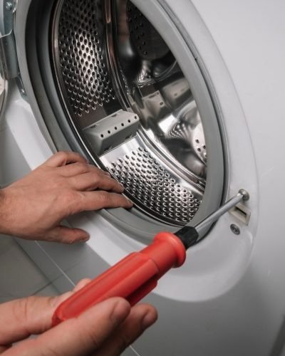 Technician using a screwdriver to repair a washing machine drum bearing