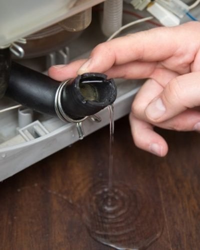 Technician inspecting a leaking washing machine drain hose connection